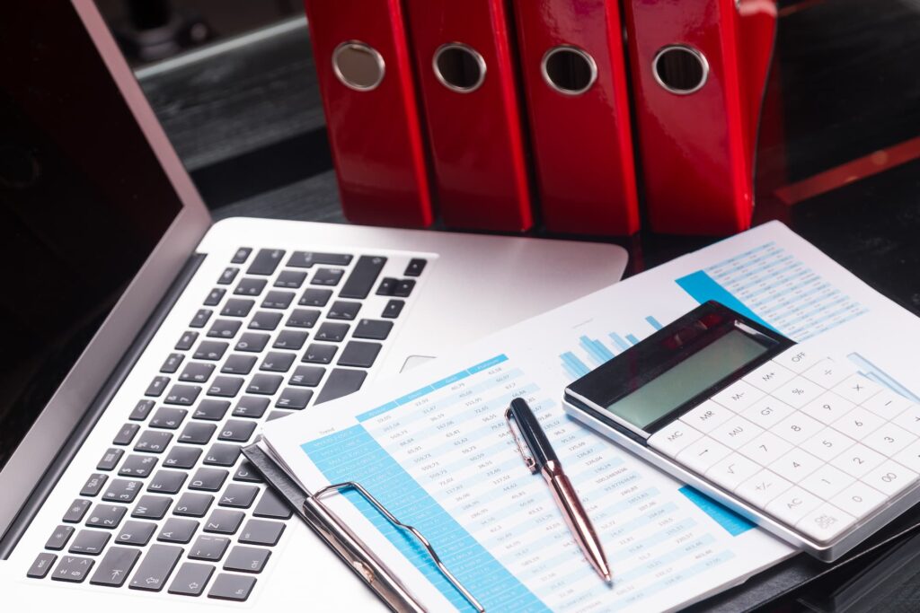 Bureau avec ordinateur portable, calculatrice et graphiques imprimés pour le suivi de la rentabilité d’une PME.